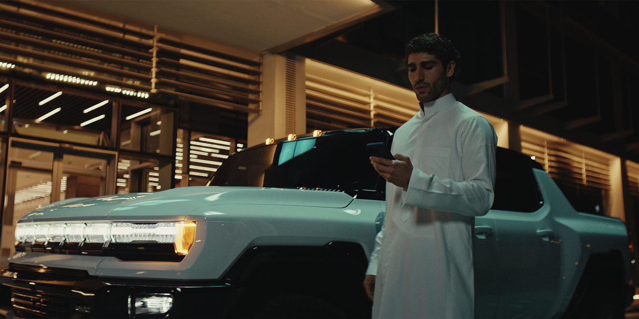 Man holding a phone next to a white coloured HUMMER EV