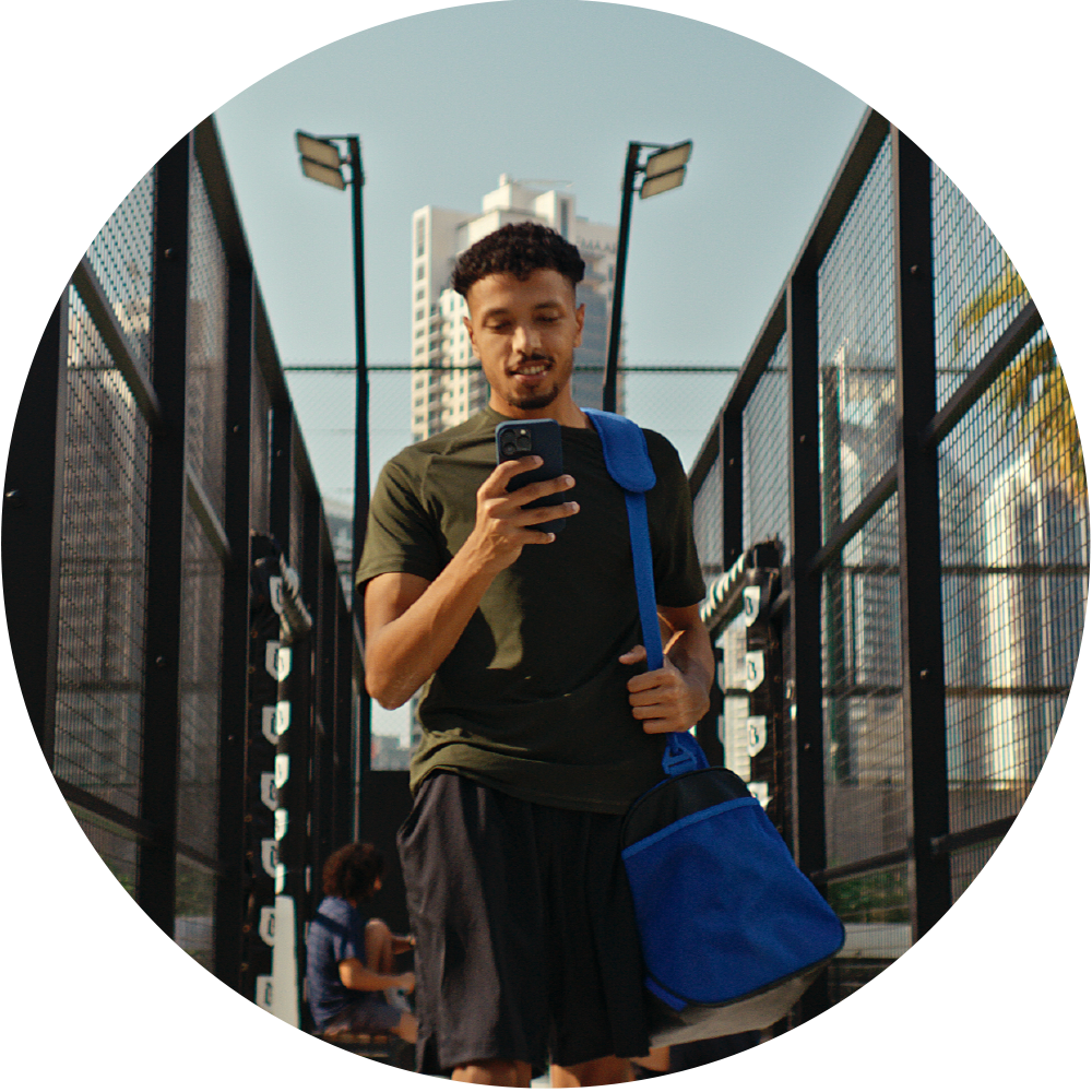 Man standing outside tennis courts in sports clothing smiling at his phone