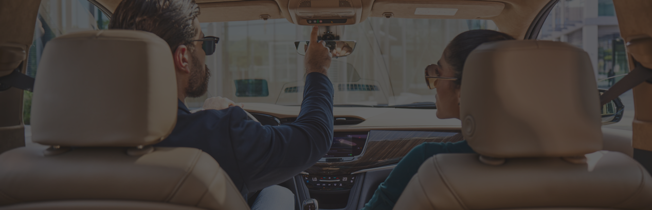 man and woman sitting inside the car and man's hand moving towards OnStar button