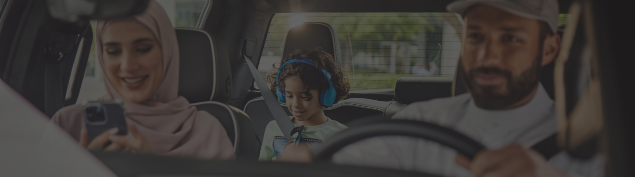 Woman looking at the phone and man beside her driving and the kid looking at the tab in the backseat