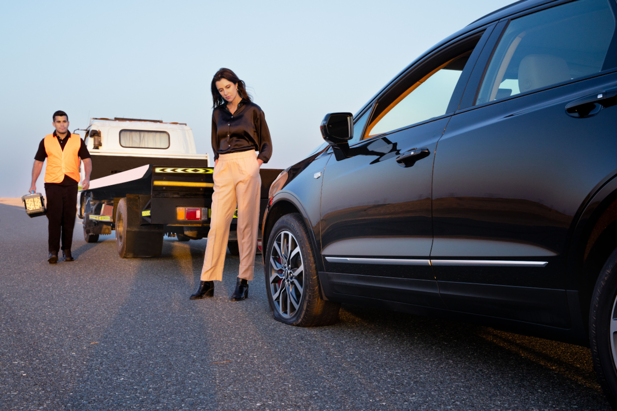 Woman standing in front of her car and man walking toward her next from a tow truck